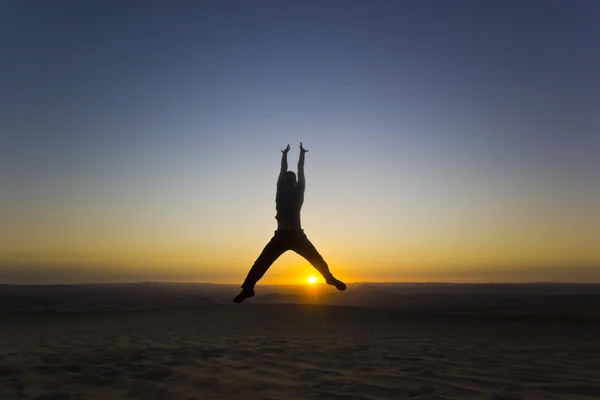 Homem saltando com as mãos para cima ao pôr do sol no deserto — Fotografia de Stock