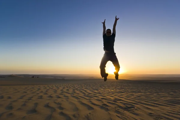 Jumping man with hands up at sunset in desert — Stock Photo, Image