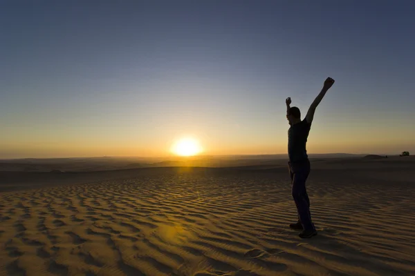 Homem de pé com as mãos para cima ao pôr do sol no deserto — Fotografia de Stock