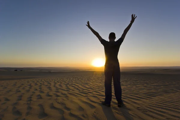 Homem de pé com as mãos para cima ao pôr do sol no deserto — Fotografia de Stock