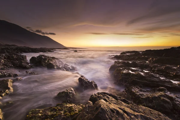 Gouden zonsondergang op de Stille Oceaan met golven op rotsachtige kust — Stockfoto