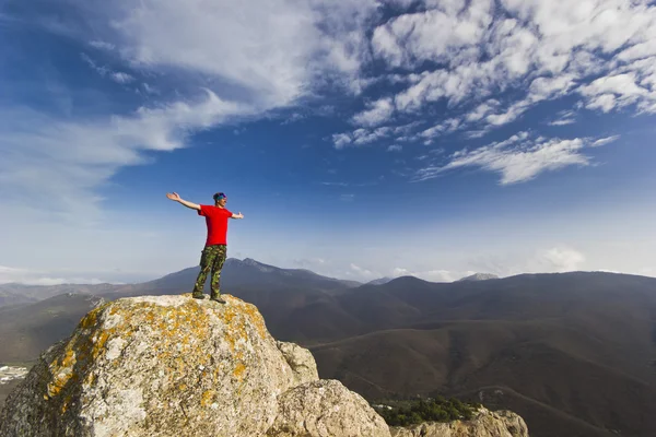 Man standing on a cliff in mountains with hands up — Stock Photo, Image