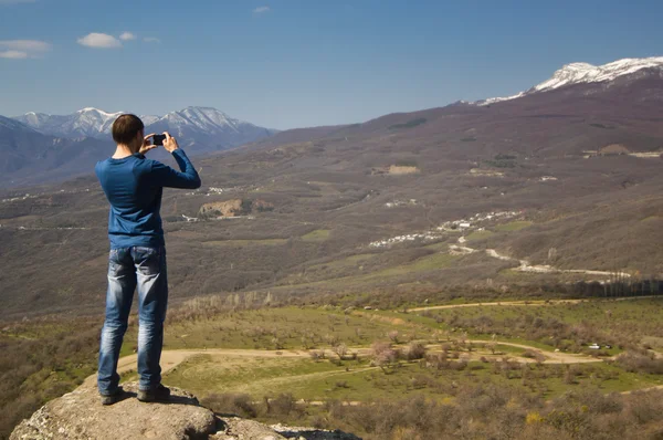 Hombre de pie en un acantilado y haciendo foto — Foto de Stock