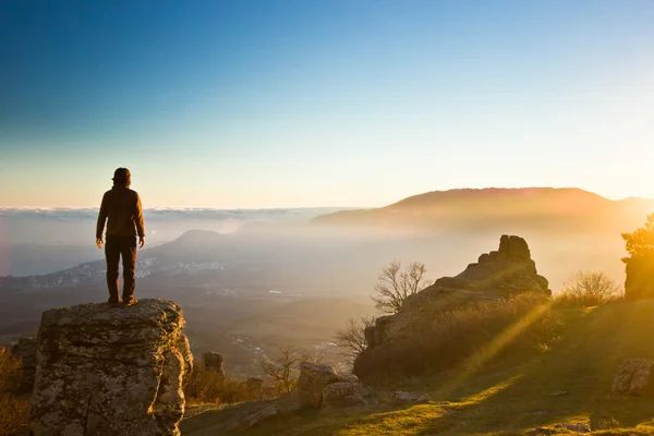 Homem no penhasco nas montanhas ao pôr do sol — Fotografia de Stock