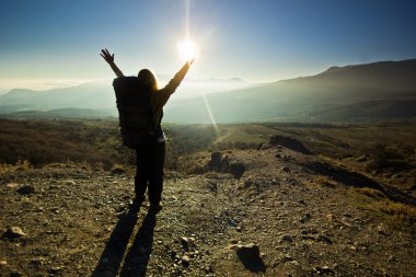 Kız-backpacker eller yukarı güneş karşı dağlarda ile