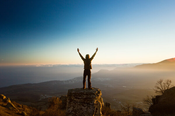 man with hands up in the mountains against sun