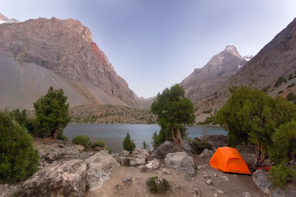 Tenda arancione vicino lago di montagna blu al tramonto — Foto Stock