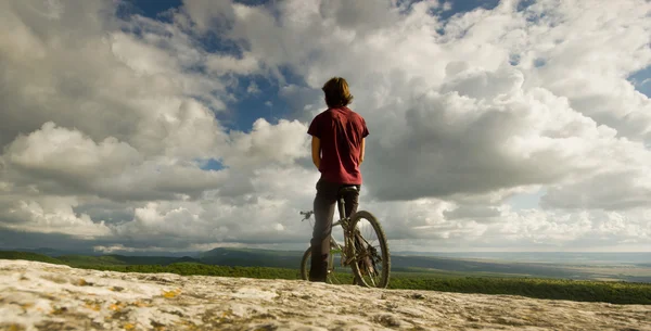 Homme à vélo près d'une falaise couverte de collines forestières — Photo