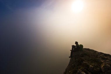 bir uçurum sisli havalarda üzerinde oturan adam