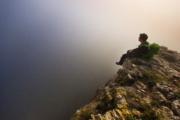 Mann sitzt bei nebligem Wetter auf einer Klippe — Stockfoto