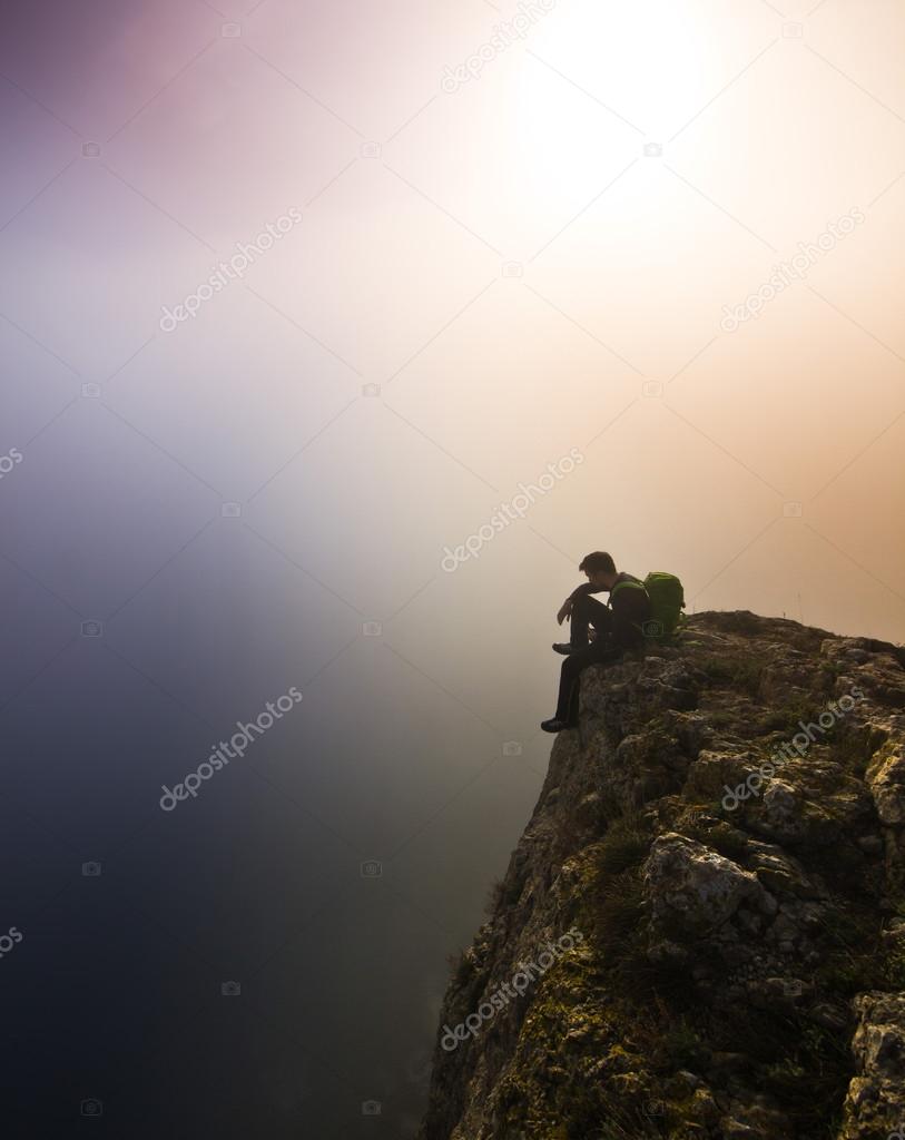 man sitting on a cliff in foggy weather