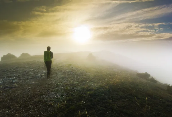 Man lopen op een heuvel in mistig weer bij zonsondergang — Stockfoto