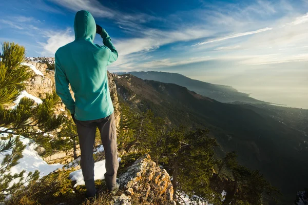 Homem de pé em um penhasco nas montanhas ao nascer do sol — Fotografia de Stock