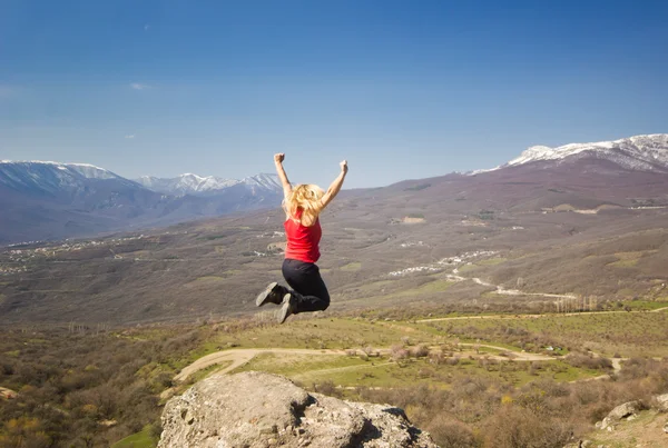 Girl jumping with hands up in the mountains against sun — Stock Photo, Image