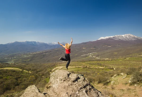 Girl jumping with hands up in the mountains against sun — Stock Photo, Image