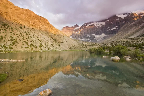 Modré horské jezero obklopené vysokými horami při západu slunce — Stock fotografie