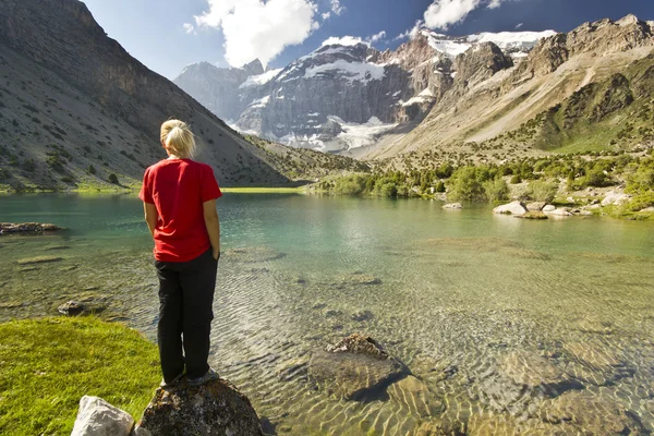 Mädchen in rotem T-Shirt steht am blauen Bergsee — Stockfoto