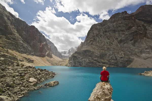 青い山の湖のそばに座って赤い t シャツの女の子 — ストック写真