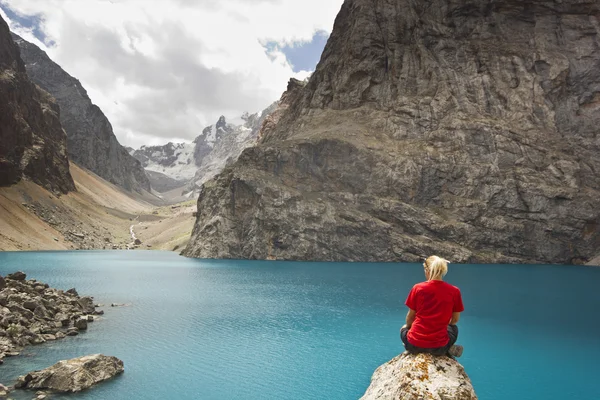 Дівчина в червоній футболці, що сидить біля блакитного гірського озера — стокове фото