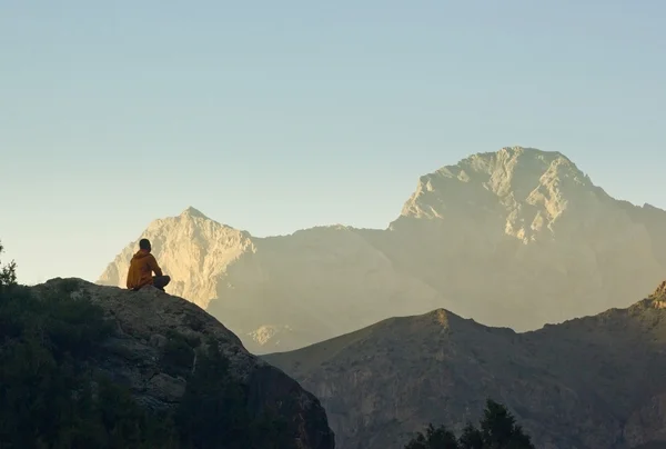 Man sitting on a cliff at sunset surrounded by mountains — Stock Photo, Image