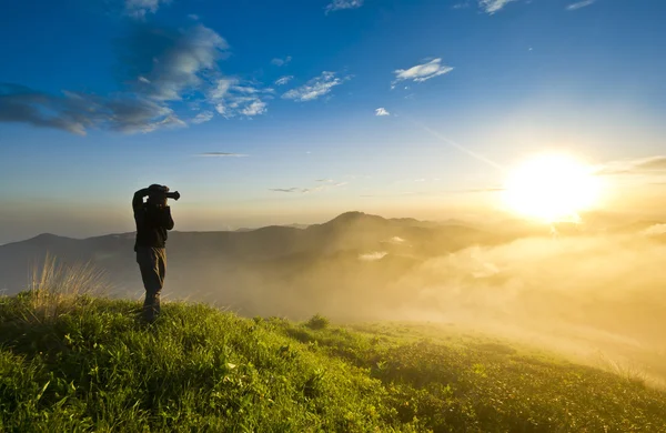 Людина на пагорбі на заході сонця з фотоапаратом, що робить фотографію — стокове фото