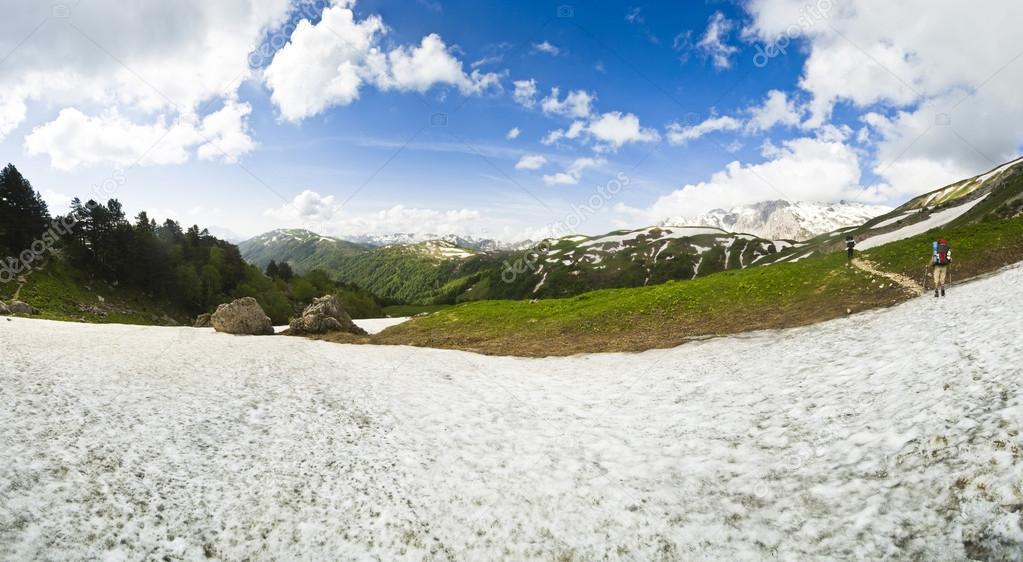 panorama of summer snow mountains with hikers on the path
