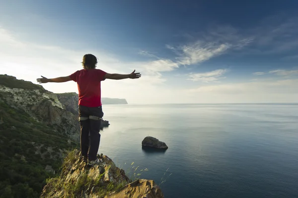 Hombre de pie en un acantilado en las montañas con las manos arriba — Foto de Stock