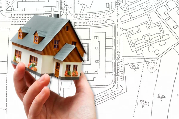 Hand met nieuwe model huis en het platform blauwdruk plan — Stockfoto