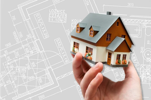 Hand holding new model house and architecture blueprint plan — Stock Photo, Image