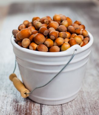 Ahşap arka plan üzerinde beyaz bir kova içinde fındık