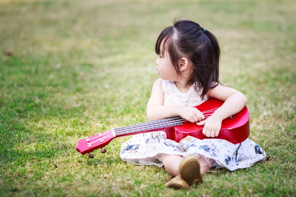 Pequeña asiática chica jugar guitarra en el jardín Imágenes de stock libres de derechos