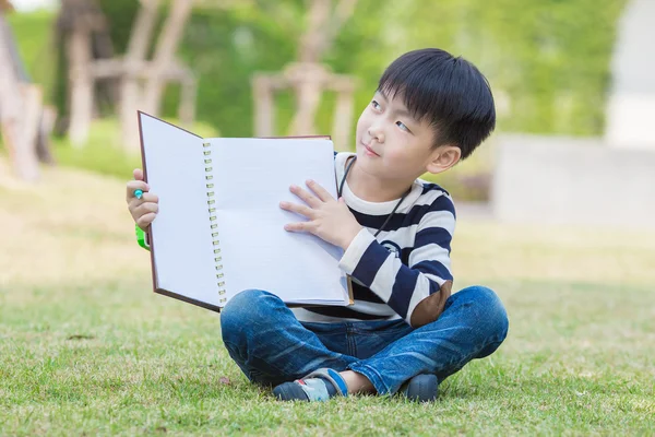 Маленький азиатский мальчик читал книгу в саду — стоковое фото