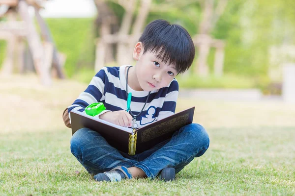 Piccolo asiatico ragazzo scrivere compiti in il giardino — Foto Stock