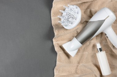 Bej renkli havlu üzerinde saç şekillendirme araçları (beyaz saç kurutma makinesi, saç spreyi)