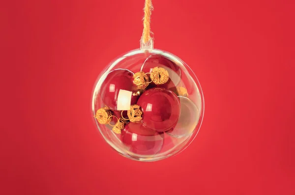 Bola transparente con bolas de navidad rojas en el interior en el fondo rojo —  Fotos de Stock