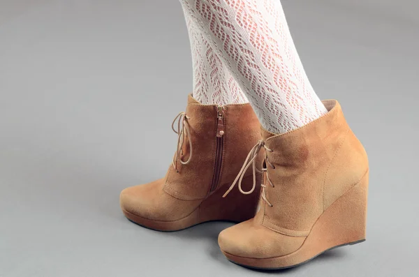Hermosas piernas femeninas en botas de gamuza marrón sobre un fondo gris —  Fotos de Stock