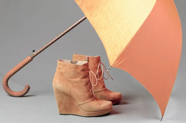 Brown suede boots under an umbrella on a gray background. Waterp