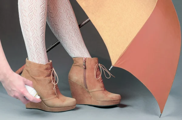 Female legs in brown suede boots under an umbrella on a gray bac — Stock Photo, Image