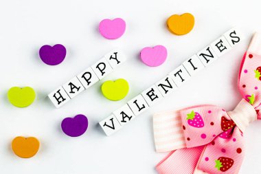 Mutlu sevgililer günü mesajları ahşap bloklardan dizilmiş beyaz bir arka planda renkli ahşap kalpler ve şirin bir yay eşliğinde.