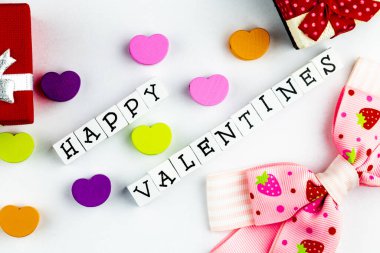 Mutlu sevgililer günü mesajları ahşap bloklardan dizilmiş beyaz bir arka planda renkli ahşap kalpler ve şirin bir yay eşliğinde.