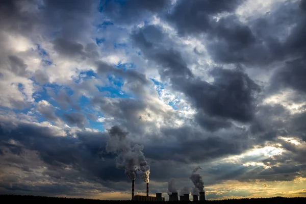 A view of the smoking chimneys of a coal-fired power plant against the backdrop of a dramatic sky with clouds. The photo was taken in natural daylight.