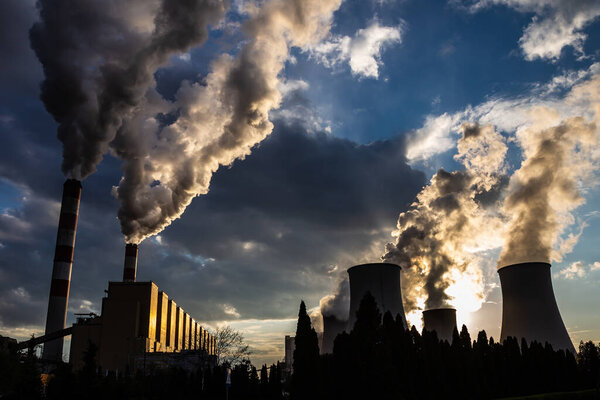 Вид дымящихся труб угольной электростанции на фоне драматического неба с облаками. Фотография сделана при естественном дневном свете.