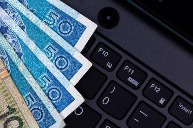 Siyah dizüstü bilgisayar klavyesine yerleştirilmiş Polonya 50 ve 100 PLN banknot seti. Fotoğraf yapay, yumuşak ışık altında çekildi