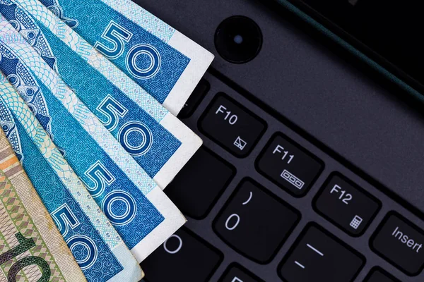 Siyah dizüstü bilgisayar klavyesine yerleştirilmiş Polonya 50 ve 100 PLN banknot seti. Fotoğraf yapay, yumuşak ışık altında çekildi