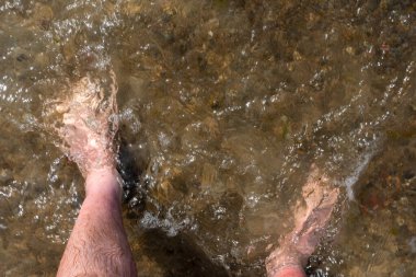  Sahilde duran bir adamın ayaklarının ilk bakışı, hafif dalgaların altında kalmış. İyi ışıklandırma koşullarında çekilmiş..