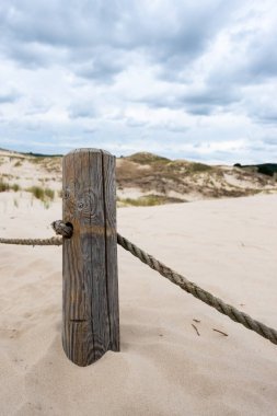 Korunan alandan yürüyüş yolunu ayıran esnek ipli tahta bir direk. Fotoğraf bulutlu bir günde iyi ışıklandırma koşullarında çekildi.