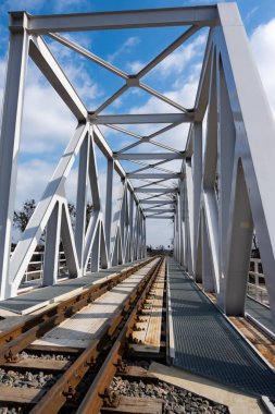 Raylara yakın çekim ve bir demiryolu köprüsü. Güneşli bir günde çekilmiş perspektif fotoğrafı.