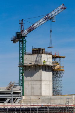 Yükseklerde çalışan işçiler bir kamu tesisi inşaatında çalışıyorlar. İnşaat vinç sapanından yapısal elementlerin toplanması. Fotoğraf güneşli bir günde çekildi. Grodzisk Mazowiecki, Polonya