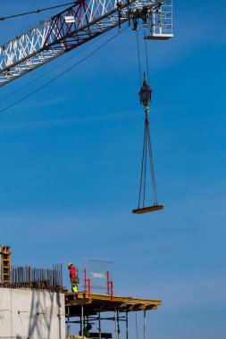 Yükseklerde çalışan işçiler bir kamu tesisi inşaatında çalışıyorlar. İnşaat vinç sapanından yapısal elementlerin toplanması. Fotoğraf güneşli bir günde çekildi. Grodzisk Mazowiecki, Polonya