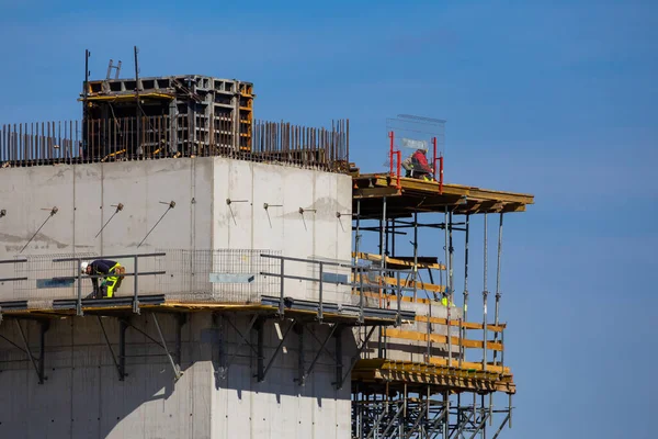 Workers working at height on the construction of a public facility. Collection of structural elements from the construction crane sling. Photo taken on a sunny day. Grodzisk Mazowiecki, Poland